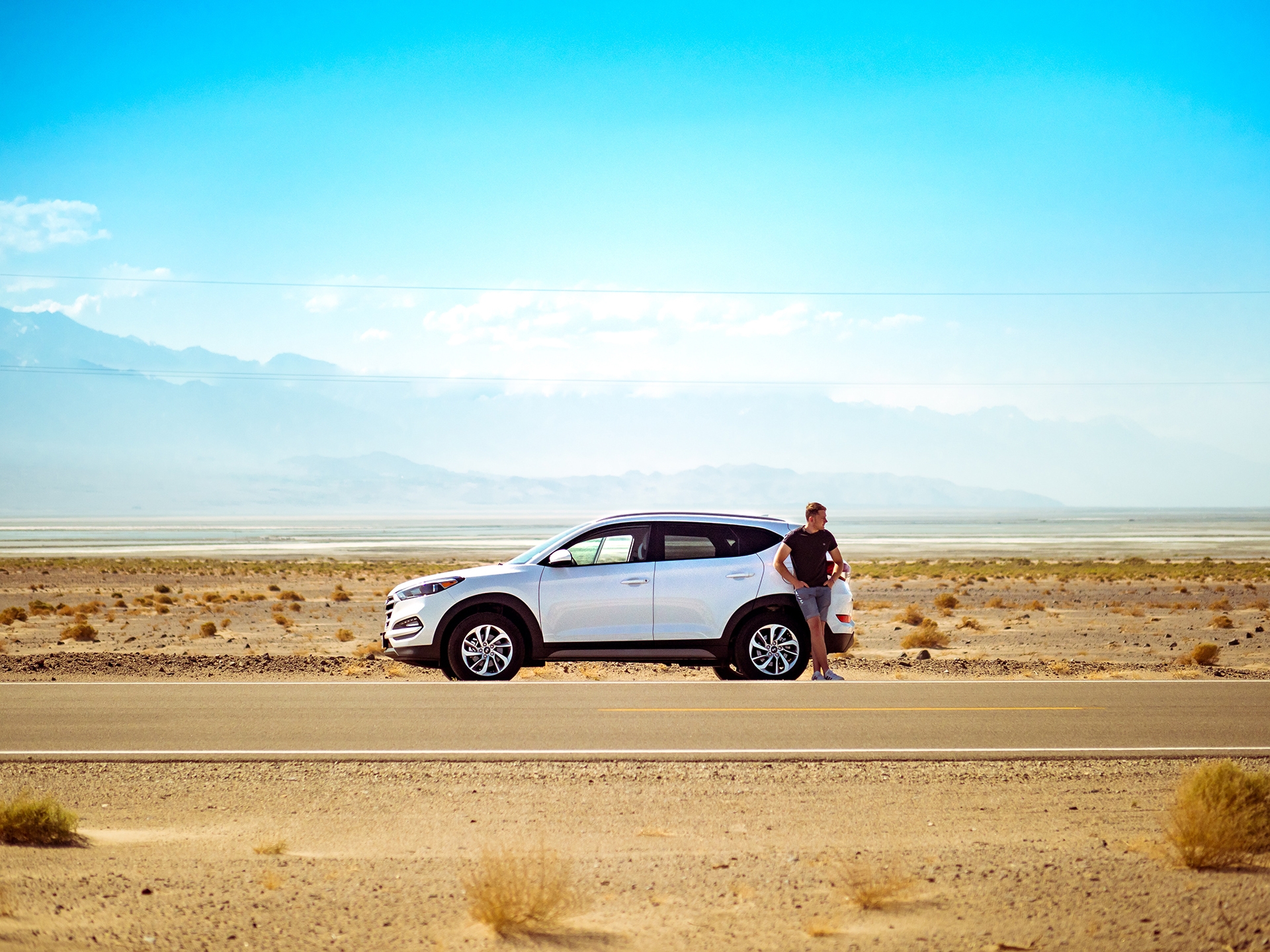 A man stands outside his broken down car on the highway, which CarGuard Administration can prevent
